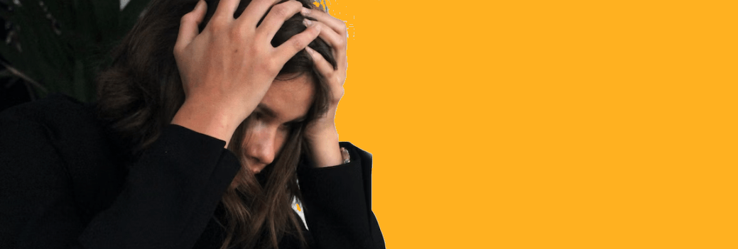 Een persoon zit met zijn handen op zijn hoofd tegen een oranje achtergrond.