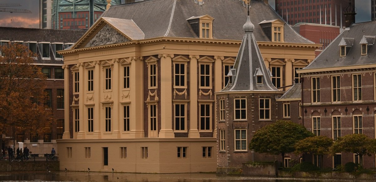 Historisch gebouw met sierlijke architectonische details aan een kanaal, omgeven door stedelijke structuren en bomen.